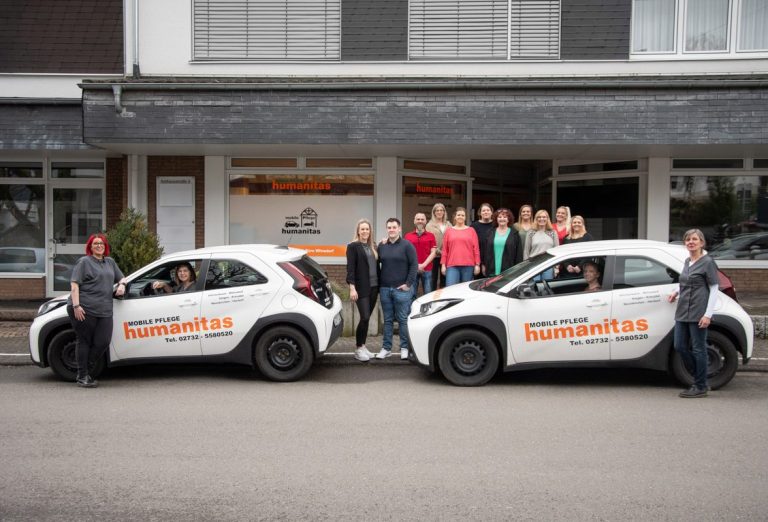 Das Team der Mobilen Pflege Humanitas Gruppenzusammenkunft vor zwei Autos mit Firmenlogo.